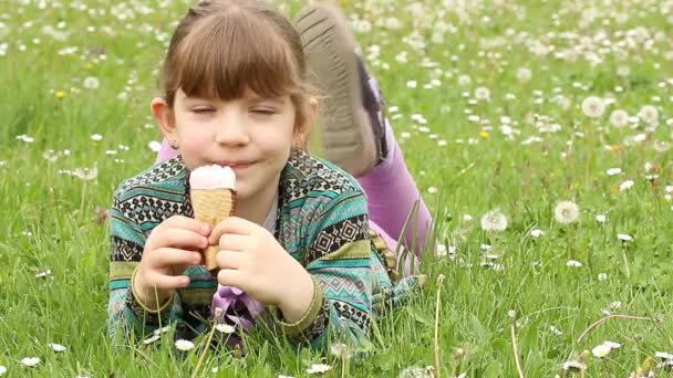 Kleines Mädchen liegt auf Gras und isst Eis — Stockvideo