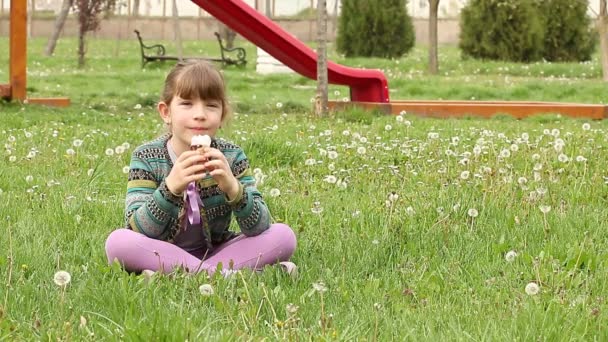 Маленькая девочка сидит на траве и ест мороженое — стоковое видео