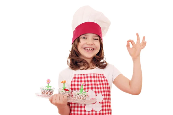 Feliz niña cocinero con flores de primavera muffins y ok mano s — Foto de Stock