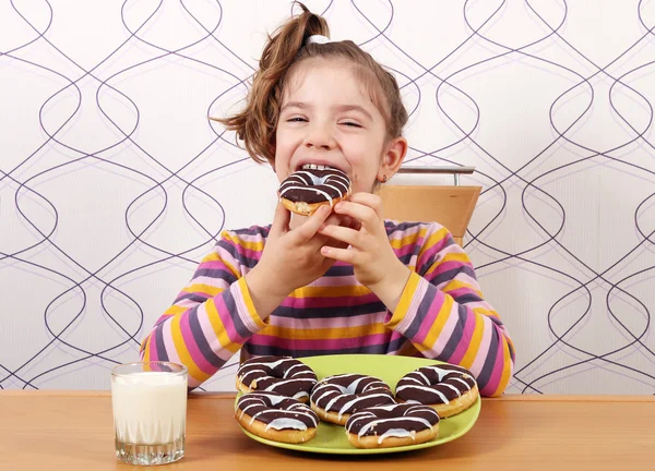 Голодная маленькая девочка ест шоколадные пончики — стоковое фото