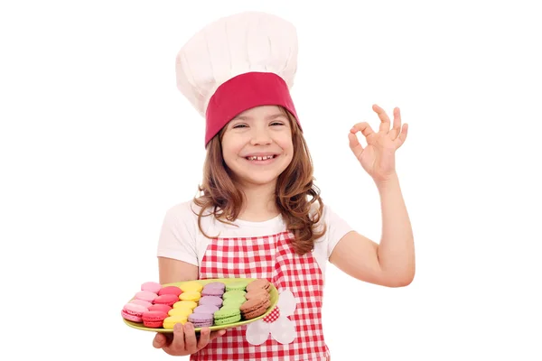 Lycklig liten flicka kock med söta macarons och ok hand tecken — Stockfoto