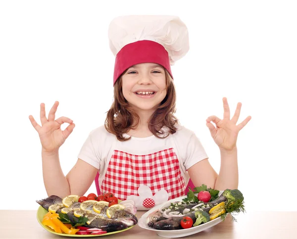 Happy little girl cook with fishes and ok hand sign — Stock Photo, Image