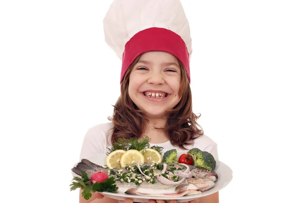 Happy little girl cook with prepared trout fish on plate — Stock Photo, Image