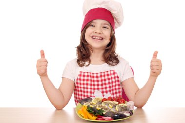 mutlu küçük kız cook balık ve başparmak yukarıya ile