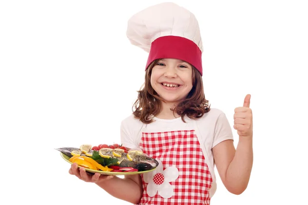 Feliz niña cocinero con preparado trucha y pulgar hacia arriba — Foto de Stock