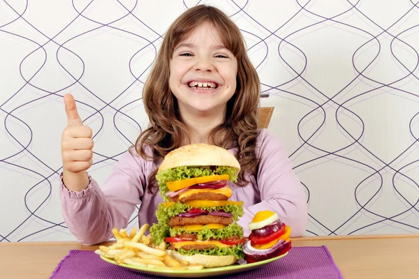 Happy little girl with big hamburger and thumb up — Stock Photo, Image