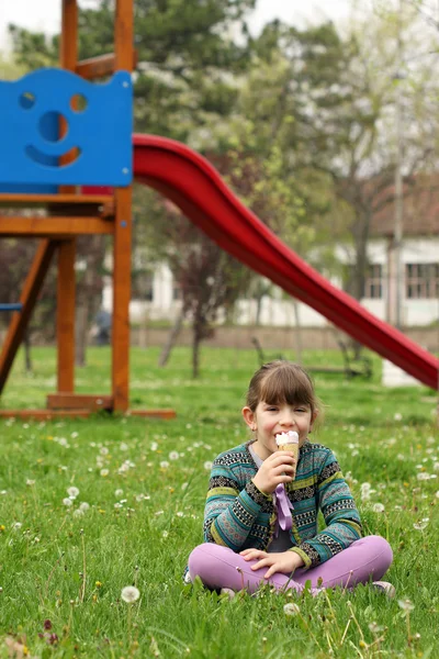 Gelukkig meisje, zittend op het gras en ijs eten — Stockfoto