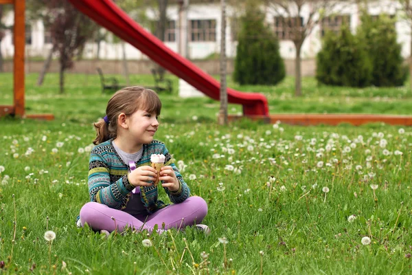 Happy little girl sitting on grass with ice cream — Stock Photo, Image