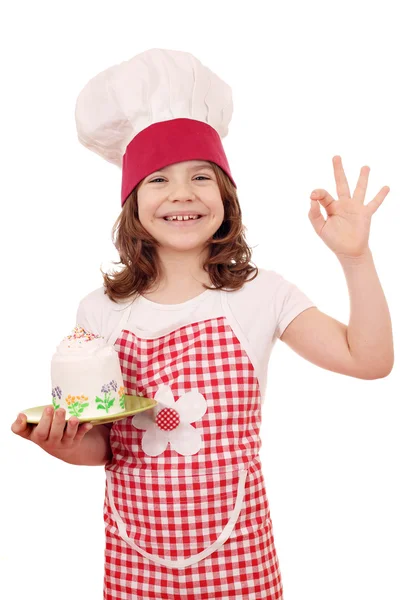 Happy little girl cook with cake and ok hand sign — Stock Photo, Image