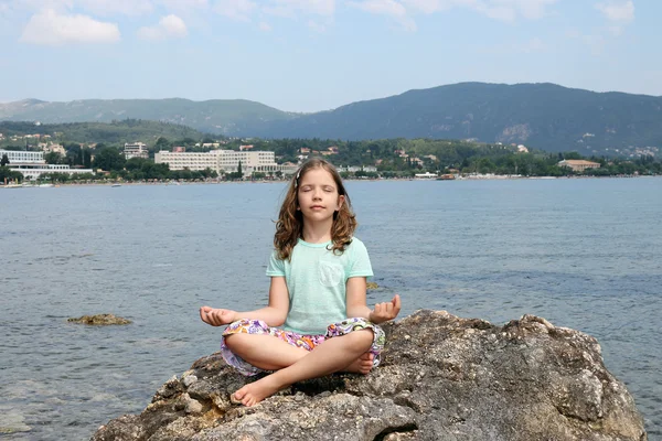 Niña sentada en una roca junto al mar y medita — Foto de Stock