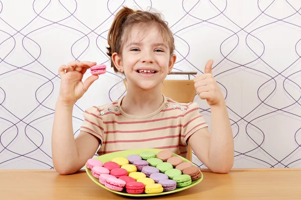 Happy little girl with macaroons and thumb up — Stock Photo, Image