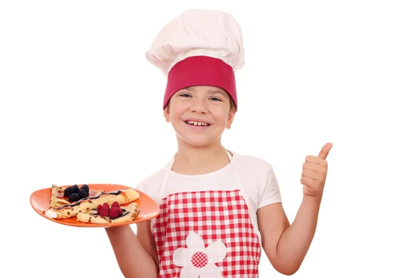 Happy little girl cook with crepes and thumb up — Stock Photo, Image