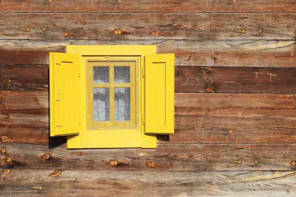 Žluté okno na zdi dřevěné chaty — Stock fotografie