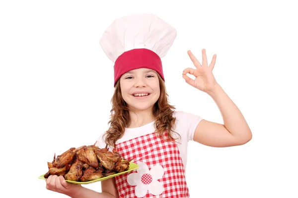 Heureuse petite fille cuisinier avec des ailes de poulet rôti et ok main si — Photo