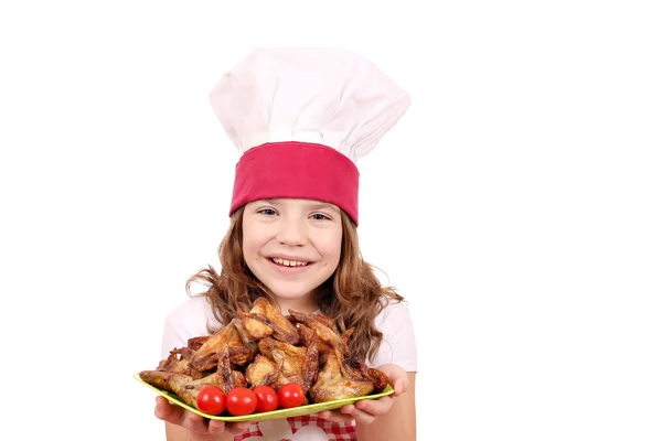 Happy little girl cook with roasted chicken wings on plate — Stock Photo, Image