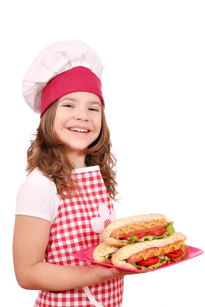 Happy little girl cook with hot dogs on plate — Stock Photo, Image