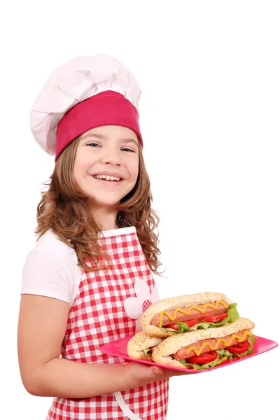 Menina feliz cozinhar com cachorros quentes no prato — Fotografia de Stock