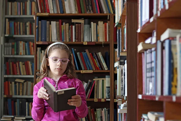 Liten flicka läser en bok i biblioteket — Stockfoto