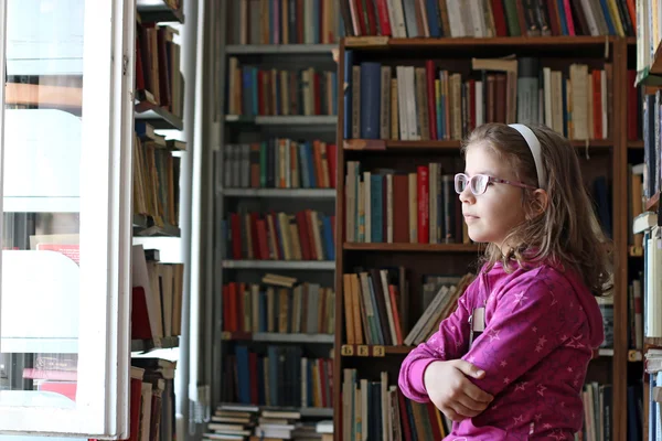 Liten flicka med bok i biblioteket — Stockfoto