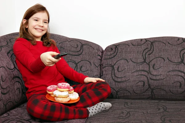 Little girl watching tv and eating donuts — Stock Photo, Image