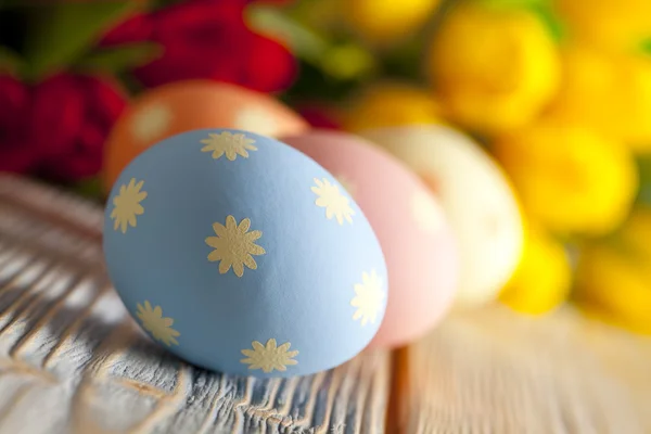 Πολύχρωμα Πασχαλινά αυγά, κόκκινες και κίτρινες τουλίπες στο παρασκήνιο — Φωτογραφία Αρχείου