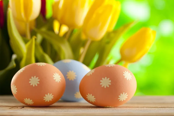 Tre uova di Pasqua sul tavolo di legno e tulipani freschi — Foto Stock