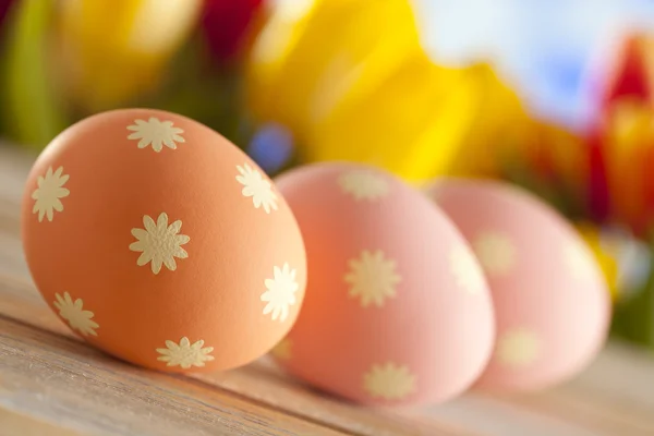 Три великодні яйця на дерев'яному столі і барвисті тюльпани на фоні — стокове фото