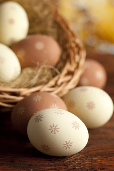 Easter eggs and wicker basket on wooden table — Stock Photo, Image