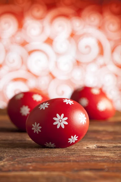 Huevos rojos de Pascua sobre mesa de madera y fondo estampado —  Fotos de Stock