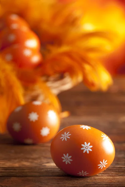 Orange påsk ägg och fjädrar på träbord — Stockfoto