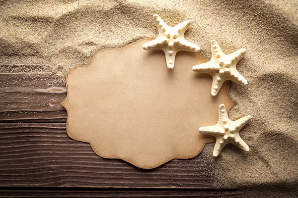 Tarjeta de papel en blanco y estrellas de mar sobre arena y mesa de madera — Foto de Stock