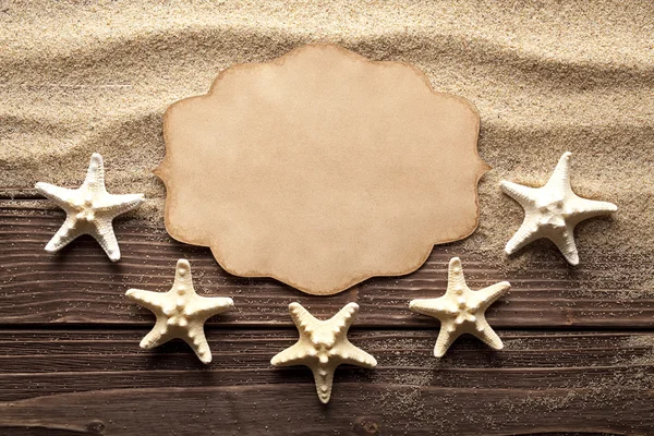 Blank paper label and starfishes on sand and wooden table — Stock Photo, Image