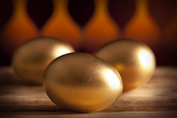 Three golden eggs on wooden table and brown background