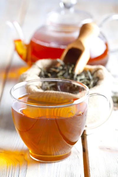 Xícara de chá, folhas de chá e bule na mesa de madeira — Fotografia de Stock