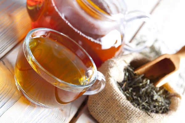 Tasse Tee, Teekanne und getrocknete Teeblätter auf Holzplanken — Stockfoto