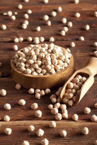 Chickpeas in bowl and scoop on wooden table — Stock Photo, Image