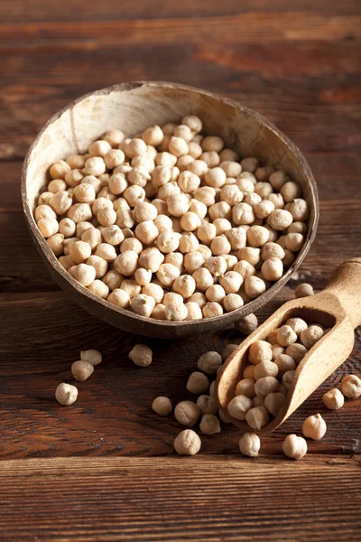 Chickpeas in bowl and scoop on wooden table — Stock Photo, Image