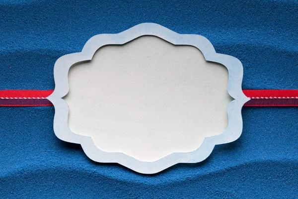 Paper label and red ribbon on blue sand background