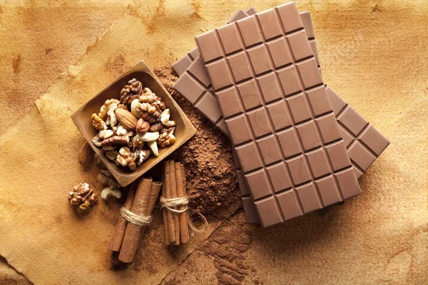 Quatro barras de chocolate, paus de canela, cacau e nozes mistas em um — Fotografia de Stock