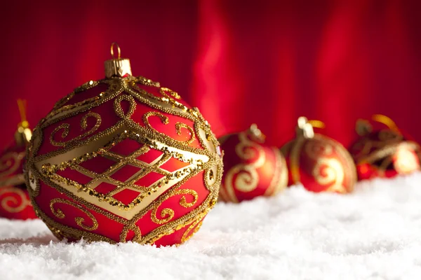 Rote Christbaumkugeln auf Schnee und rotem Hintergrund — Stockfoto