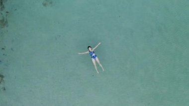 Güzel genç bir kadın yüzüyor, berrak okyanusta bir su yüzeyinde yatıyor.