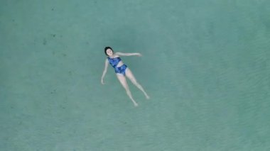 Güzel genç bir kadın yüzüyor, berrak okyanusta bir su yüzeyinde yatıyor.