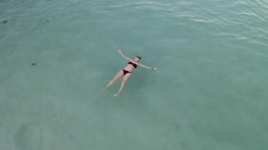 Güzel genç bir kadın yüzüyor, berrak okyanusta bir su yüzeyinde yatıyor.