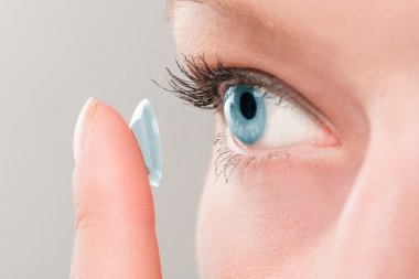 Woman inserting a contact lens in eye. clipart