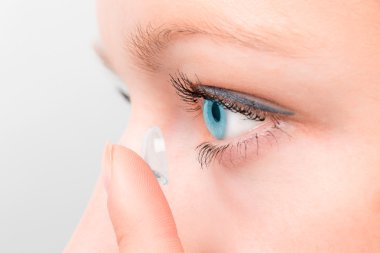 Woman inserting a contact lens in eye. clipart