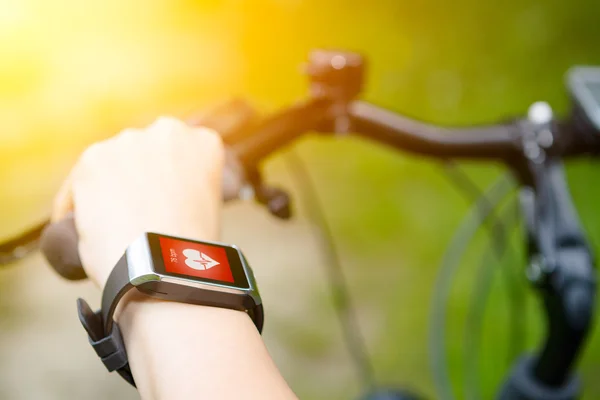 Donna in bicicletta con uno smartwatch cardiofrequenzimetro . — Foto Stock