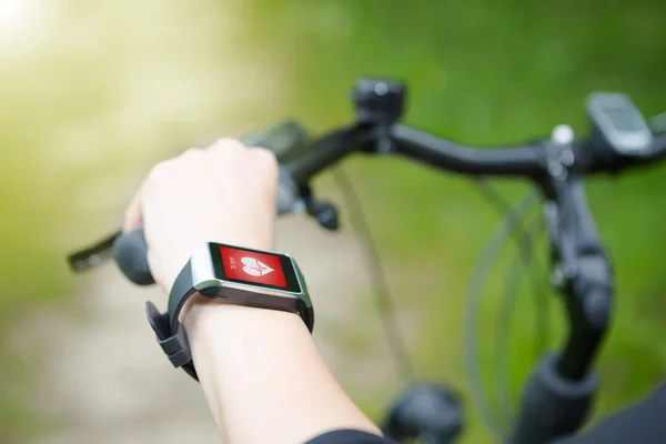 Mulher andando de bicicleta com um monitor de frequência cardíaca smartwatch . — Fotografia de Stock