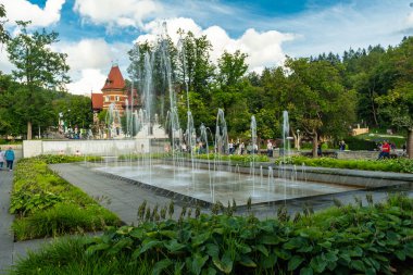Polonya 'nın Krynica Zdroj kentindeki güzel manzaralı Spa Park manzarası. Modern doğrusal fıskiyeler ve parlak bir yaz gökyüzü altında kırmızı çatıları olan tarihi tatil köyleri. Seyahat ve rahatlama için ideal..