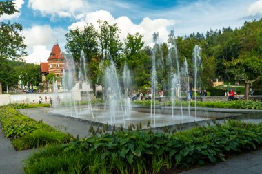 Polonya 'nın Krynica Zdroj kentindeki güzel manzaralı Spa Park manzarası. Modern doğrusal fıskiyeler ve parlak bir yaz gökyüzü altında kırmızı çatıları olan tarihi tatil köyleri. Seyahat ve rahatlama için ideal..