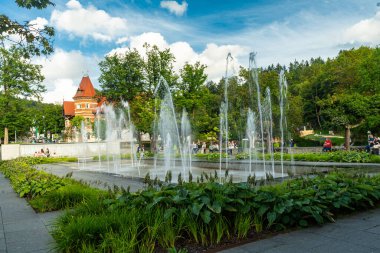 Polonya 'nın Krynica Zdroj kentindeki güzel manzaralı Spa Park manzarası. Modern doğrusal fıskiyeler ve parlak bir yaz gökyüzü altında kırmızı çatıları olan tarihi tatil köyleri. Seyahat ve rahatlama için ideal..